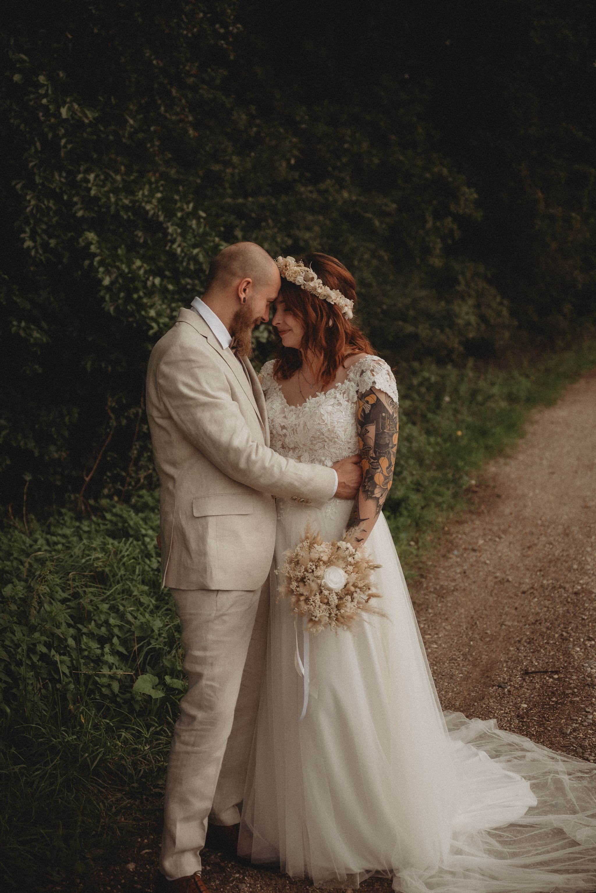 Romantic wedding portrait on dirt path with natural greenery backdrop.