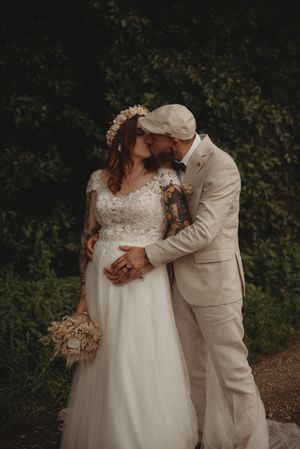 Romantic wedding couple share an intimate moment in a moody garden setting with dried floral bouquet.