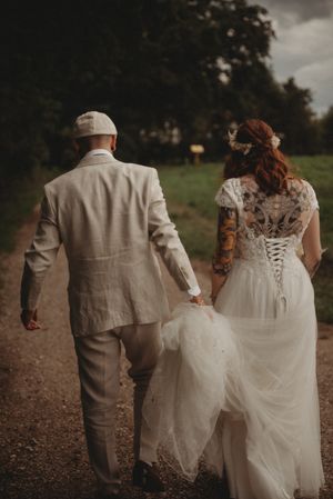 Newlyweds walk hand in hand down a rustic path showing detailed lace back wedding dress.