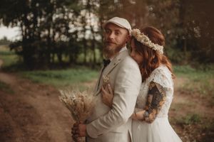 Artistic wedding portrait showing couple in beige suit and lace dress holding dried flowers.