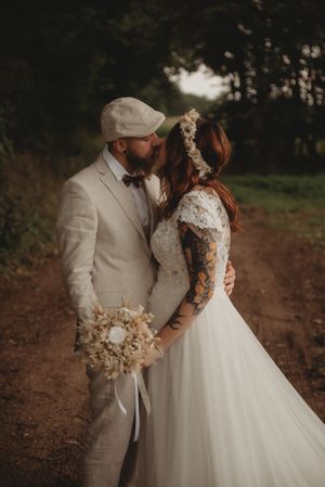 Intimate wedding photo on forest path with dried flower bouquet and beige suit.