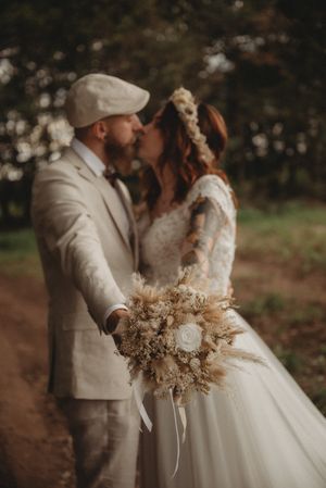 Romantic wedding portrait with dried flower bouquet and flowing white dress on forest path.