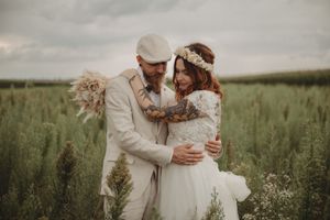 A romantic couple in light-colored wedding attire embrace in a misty field of tall grass.