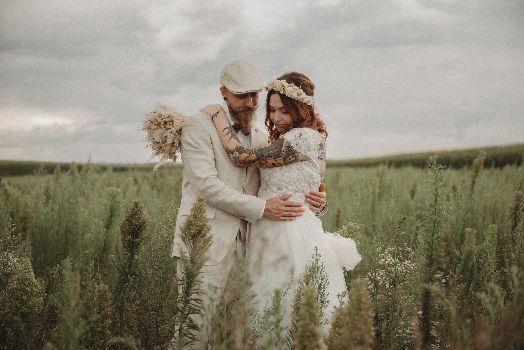 A dreamy wedding portrait of a couple in vintage-style attire standing in a meadow.