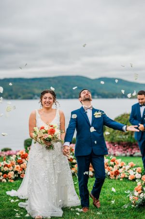 Wedding celebration at lakeside garden with flower petals being tossed as couple walks through colorful floral decor.