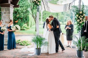 Romantic wedding ceremony under covered outdoor pavilion with blue bridesmaid dress and floral arrangements.