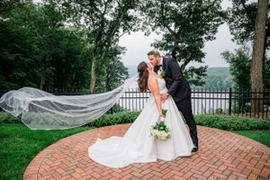 A romantic wedding moment on a brick patio overlooking verdant hills, with a flowing long veil catching the breeze.