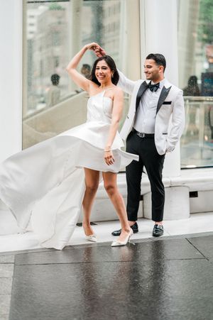 Bride in white mini dress twirls as groom in white tuxedo jacket spins her on a rainy wedding day in New York City