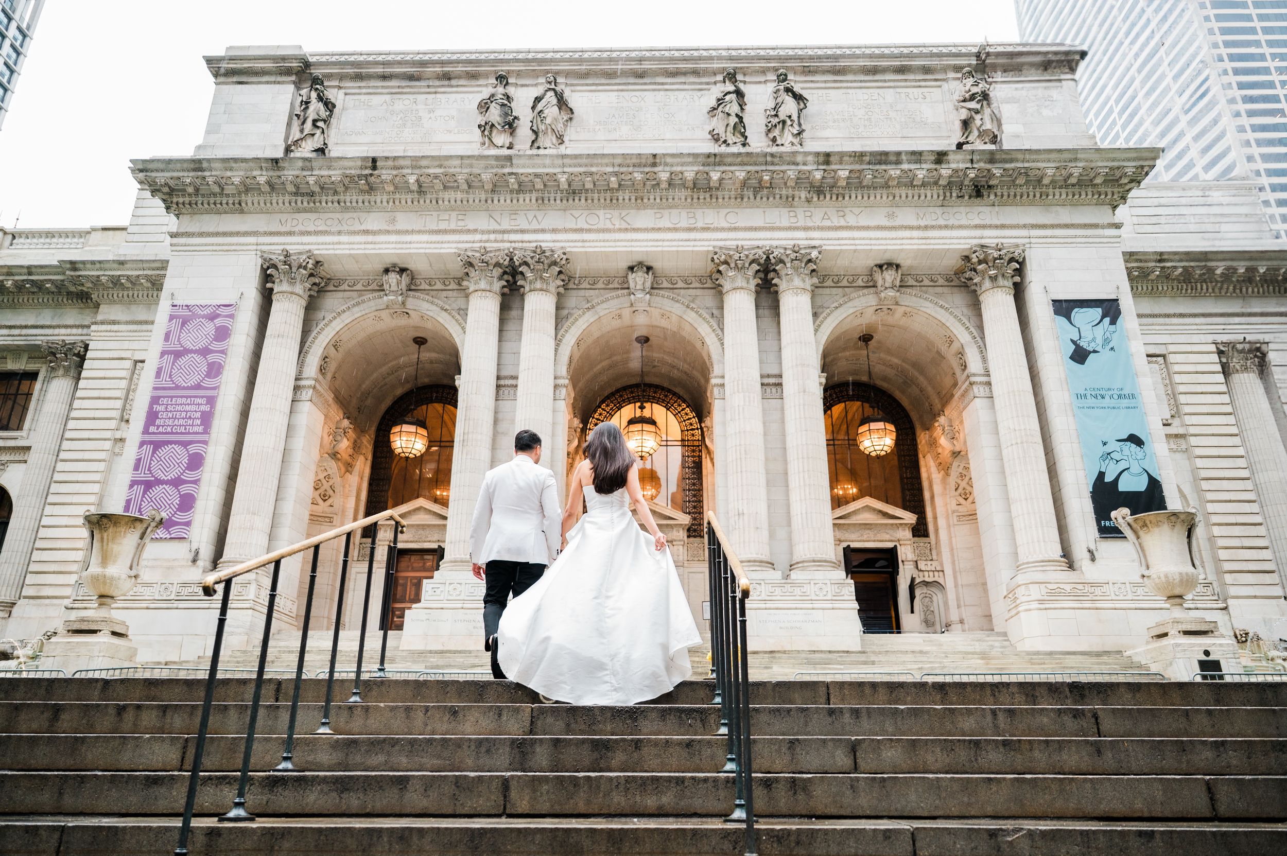 Bride and groom ascending steps of New York Public Library in wedding attire, classic Beaux-Arts architecture backdrop.