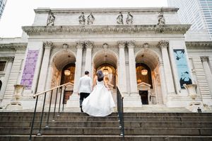 Bride and groom ascending steps of New York Public Library in wedding attire, classic Beaux-Arts architecture backdrop.
