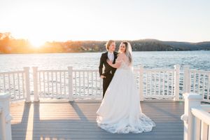 A couple shares an embrace on a waterfront dock during sunset as light glimmers across the lake.