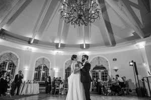 Bride and groom share first dance under elegant chandelier in grand ballroom at wedding reception at Great River Golf Club.