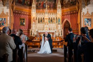 Wedding ceremony taking place inside ornate gothic church with elaborate altar and stained glass windows.