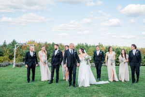 Wedding party in formal attire standing together on a lush green lawn under blue sky with white clouds at the Far at Summit Wynds, MA.