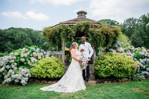 A garden wedding ceremony takes place under a decorated gazebo surrounded by blooming hydrangeas and lush greenery.