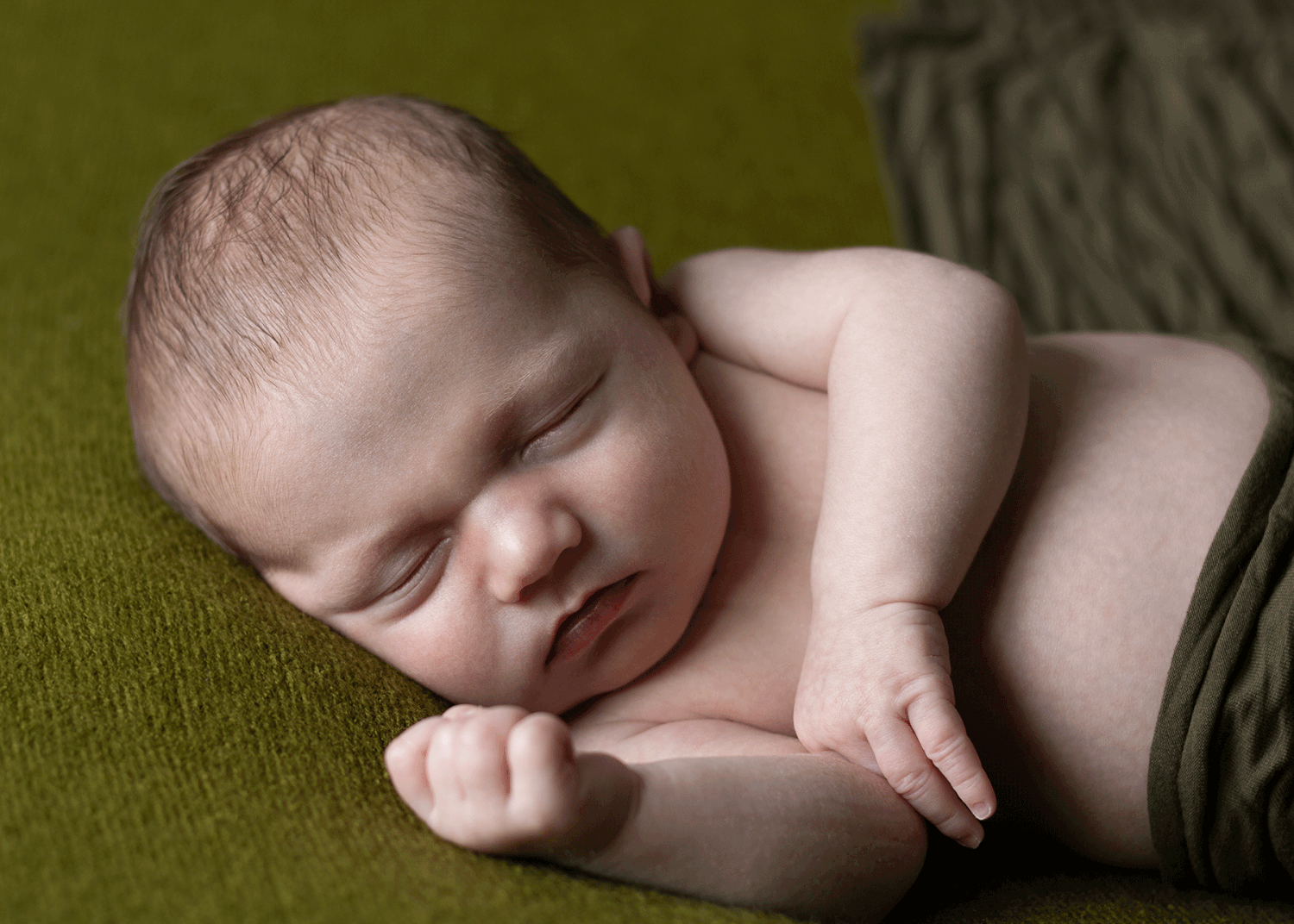 Newborn baby asleep on a green backdrop, while wrapped in a green wrap during a session with Ceredigion newborn photographer