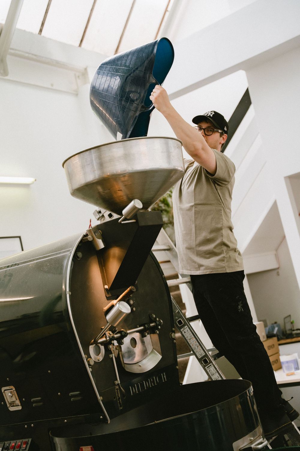 Lifestyle coffee photography in London showing a coffee roastery and a man at work pouring fresh beans into roasting machine