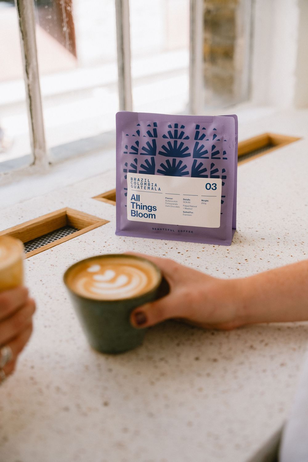 Lifestyle coffee photography in London showing a bag of All Things Bloom coffee by mug of flat white