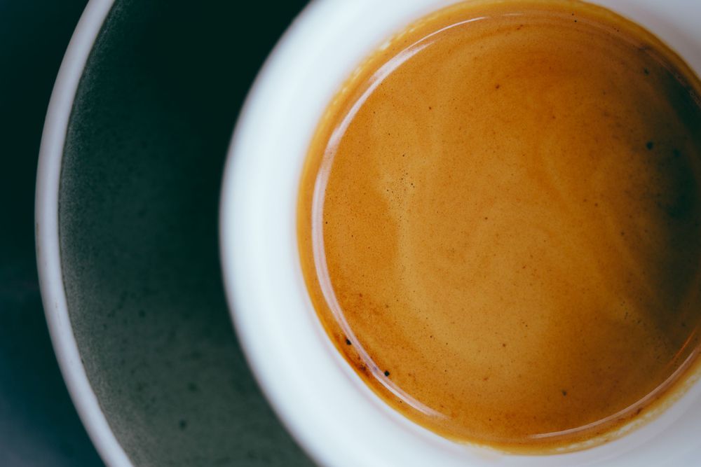 A perfectly pulled shot of espresso with rich golden crema in a white ceramic cup against a dark background.