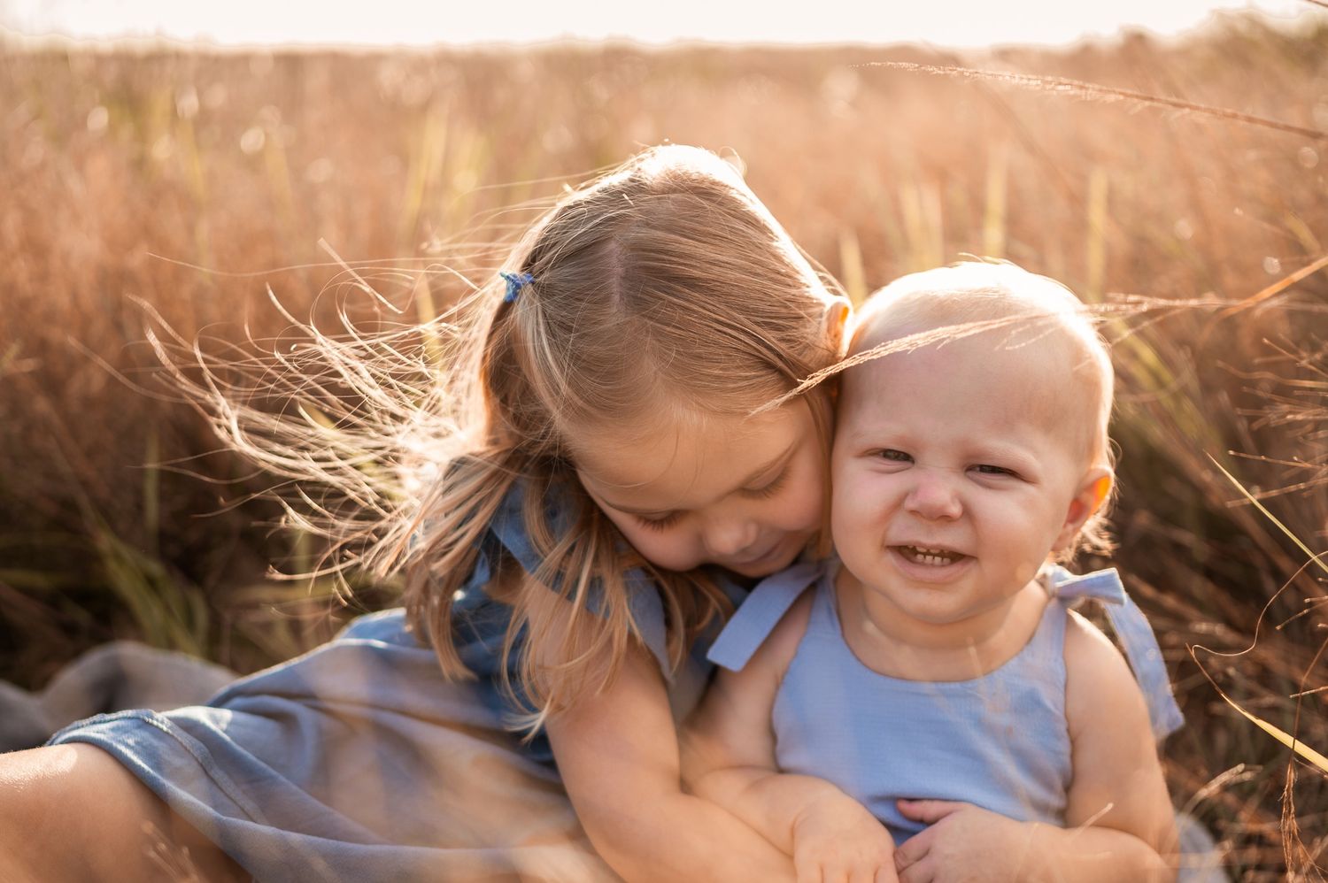 Sibling hugging at family photoshoot session in grassy field at sunset candid moment Palm Bay Melbourne Cocoa Beach Florida Brevard County