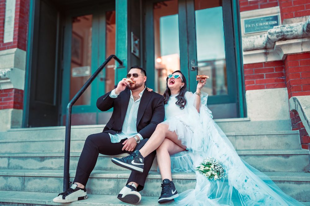 Bride and groom in edgy wedding attire sitting on brick building steps, wearing sunglasses and sneakers.