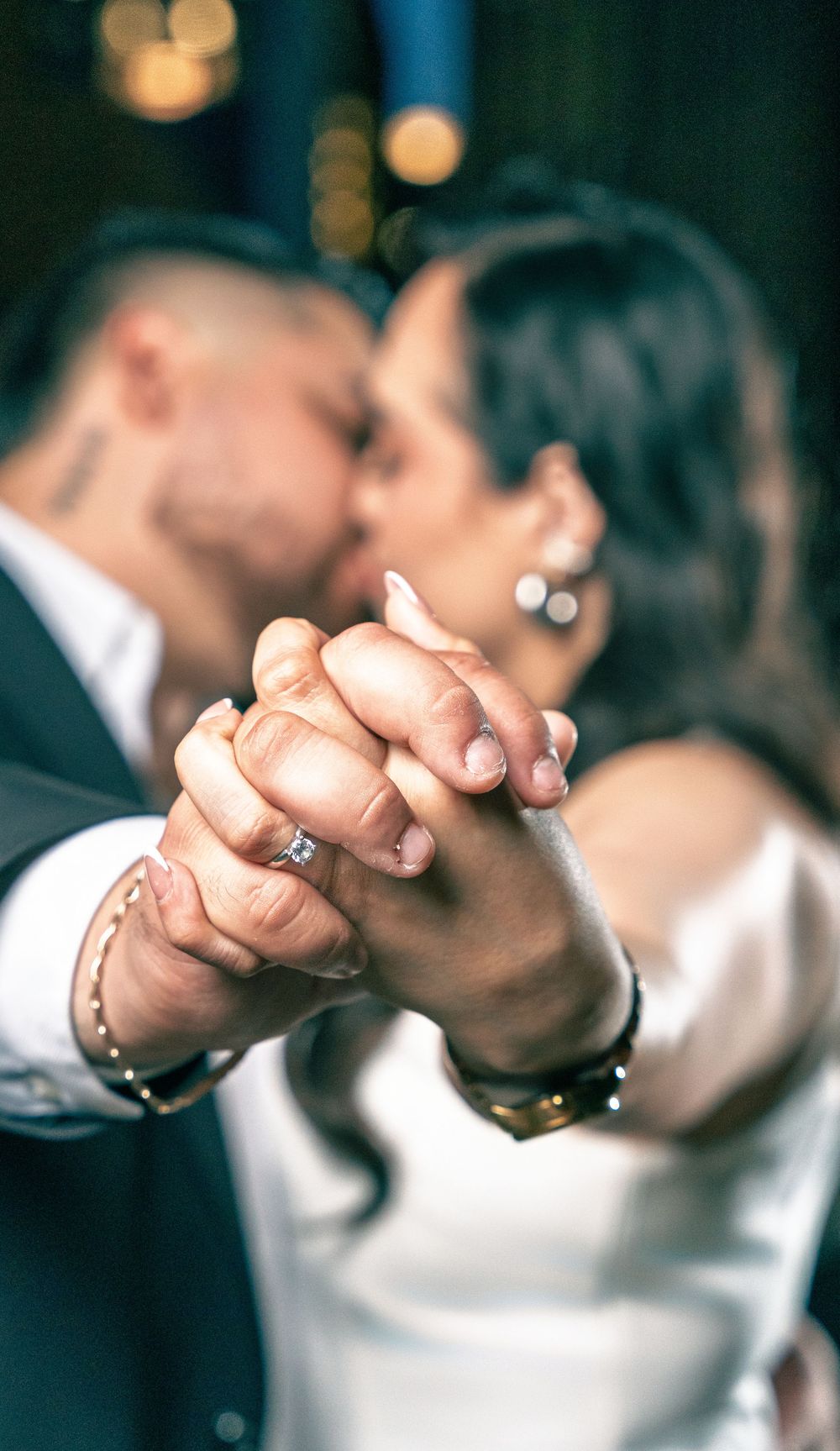Couple sharing a kiss while holding hands, showcasing an engagement ring, during their first dance at a wedding reception.