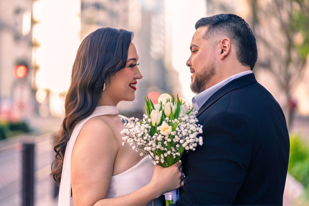 A bride and groom share a romantic moment outdoors, she holds a bouquet of white tulips and baby's breath.