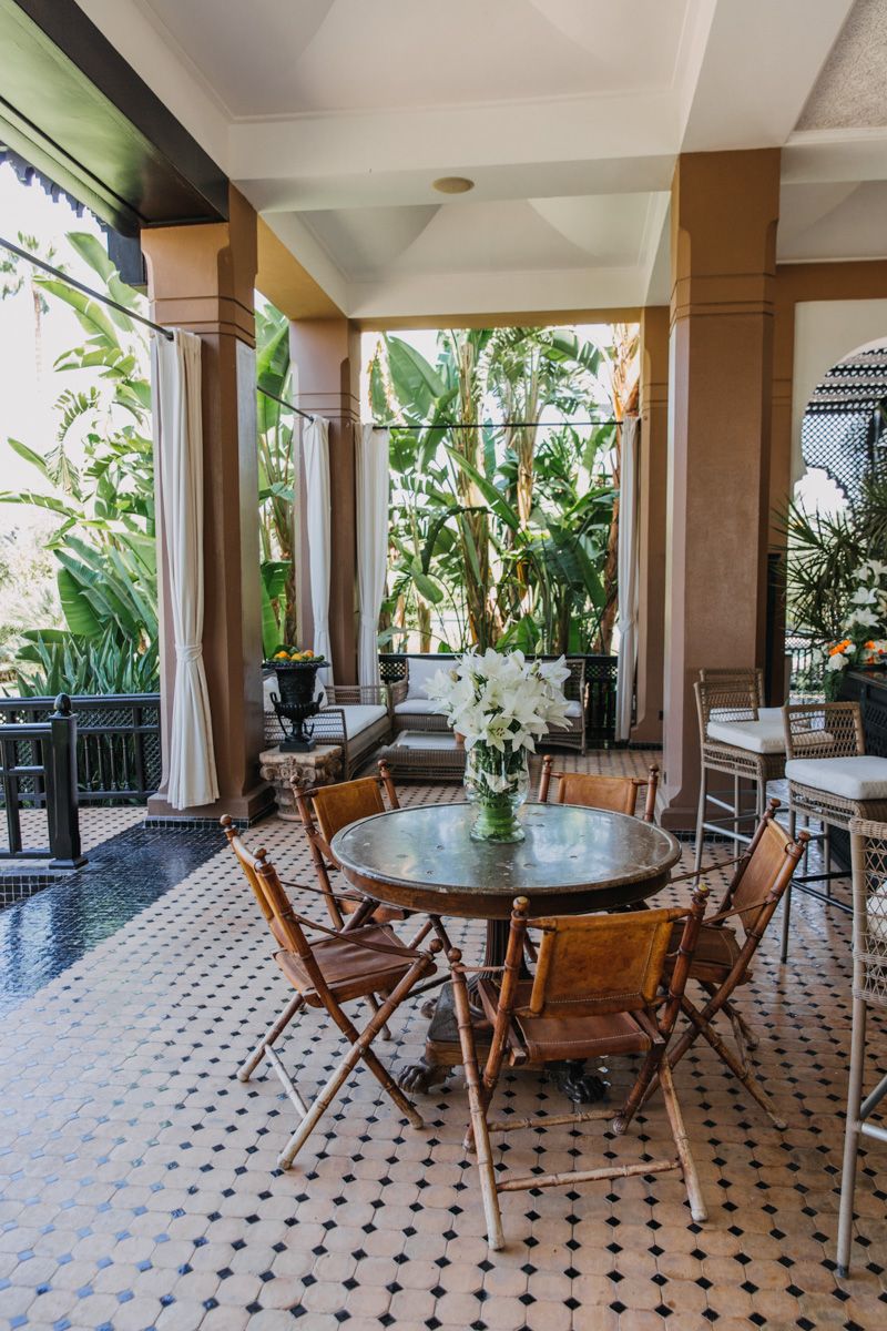 Elegant outdoor dining area with wooden furniture and tropical plants in a colonial-style setting.