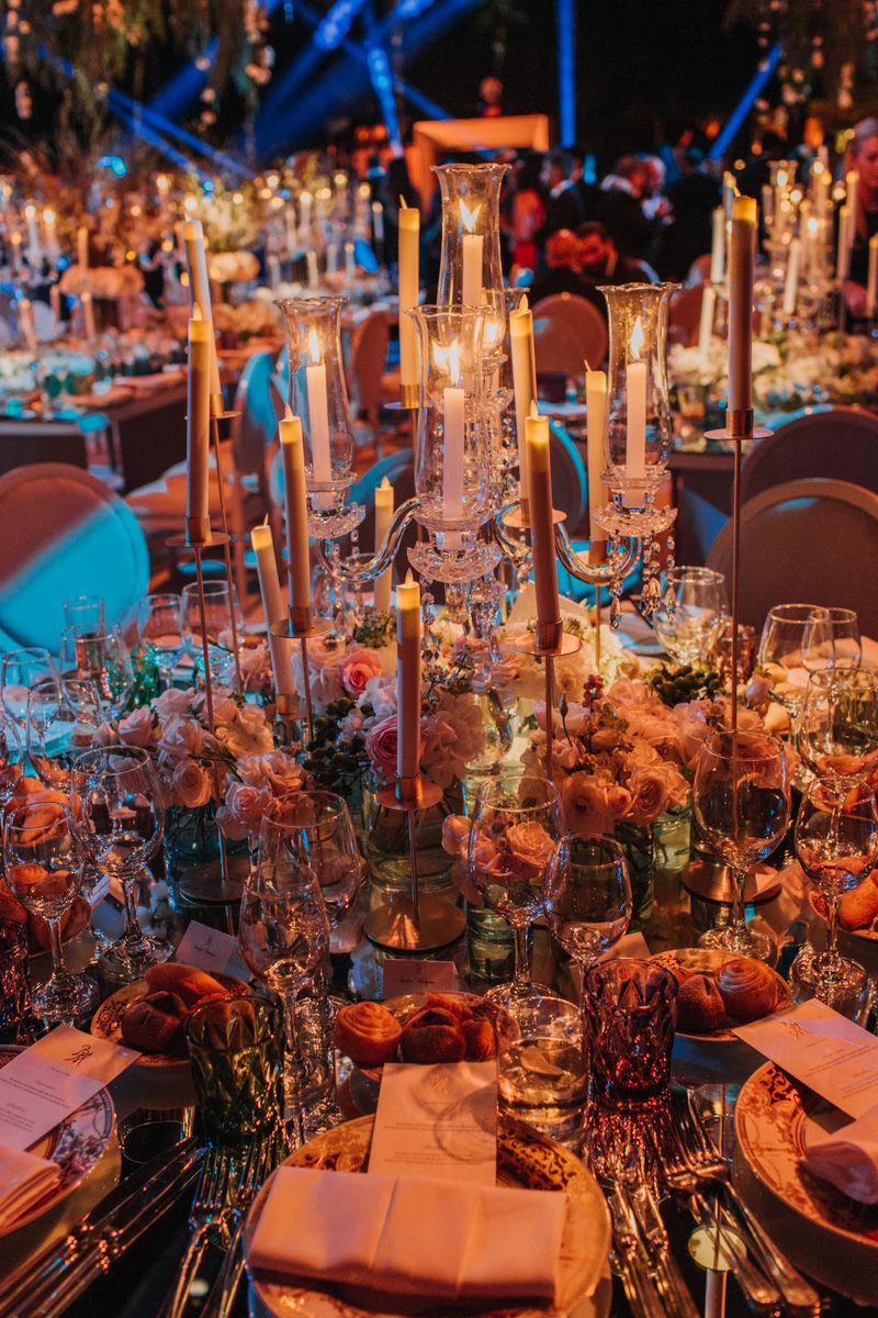 Opulent table setting features tall crystal candleholders, flowers, and fine dining arrangements.