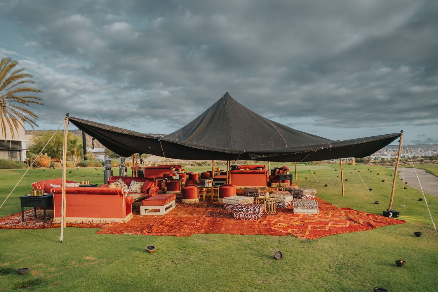 Outdoor event space with black tent canopy and red lounge seating on grass overlooking the ocean.