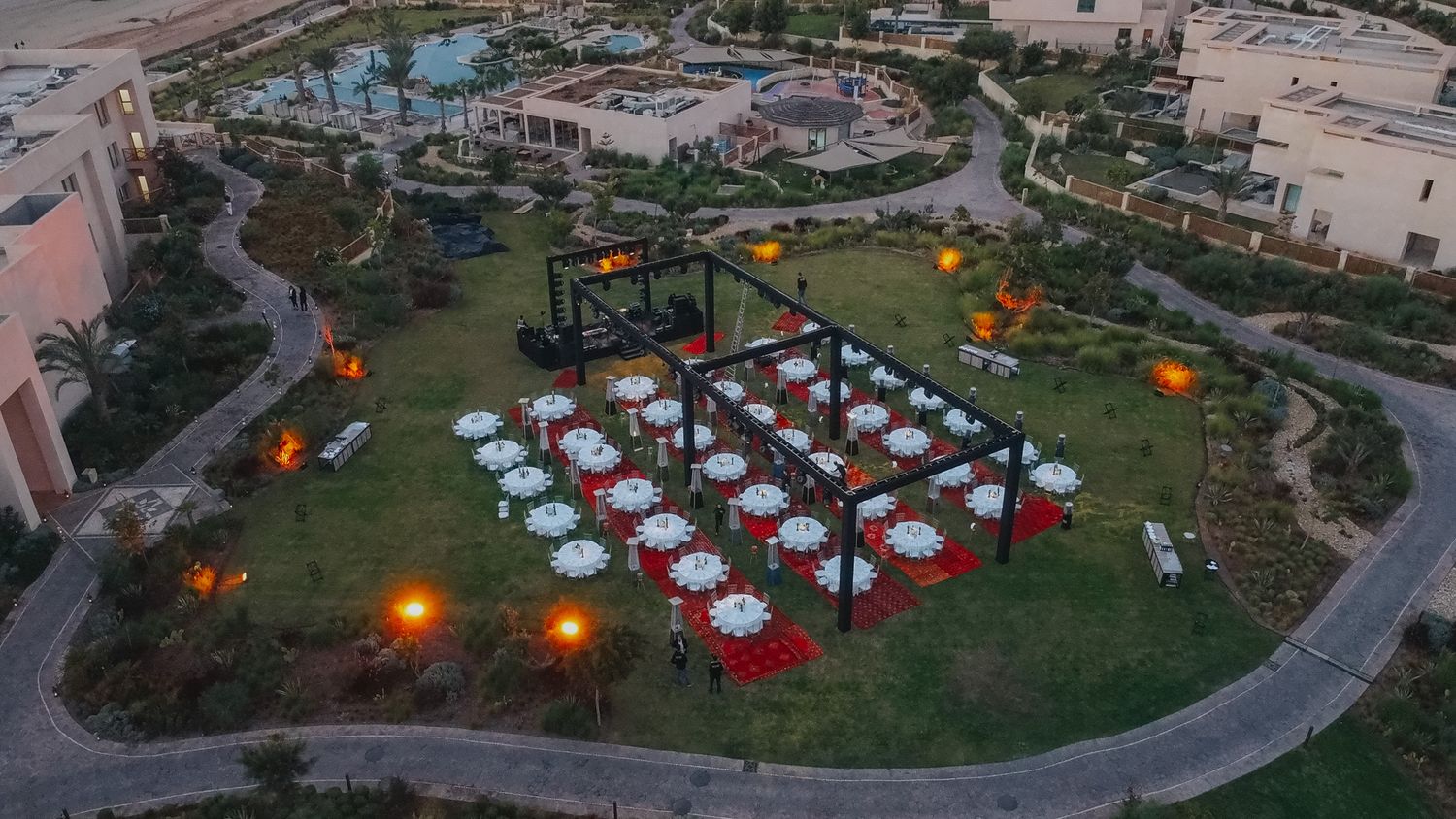 Aerial view of an outdoor event space with tables arranged under string lights at dusk.