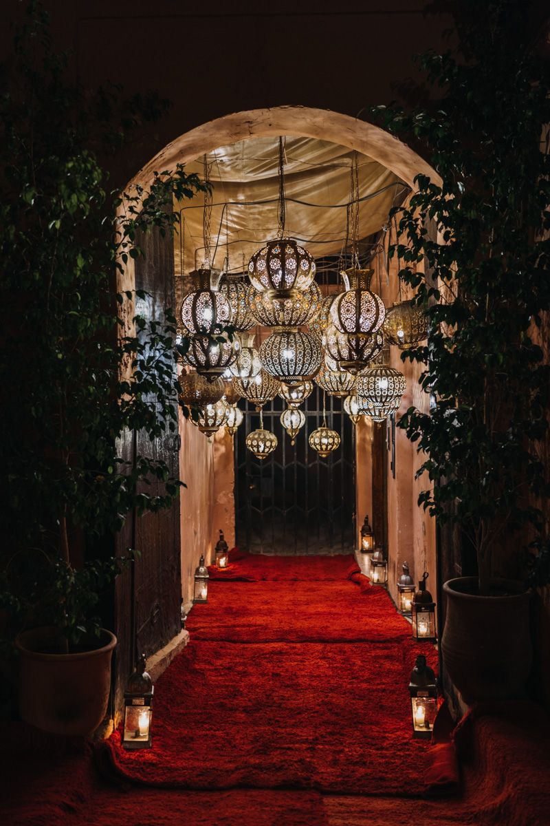 Romantic archway decorated with ornate Moroccan lanterns and a red carpet pathway lined with candles and greenery.