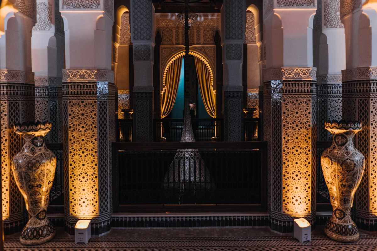 Elegant corridor with illuminated pillars and decorative vases leading to an arched doorway.