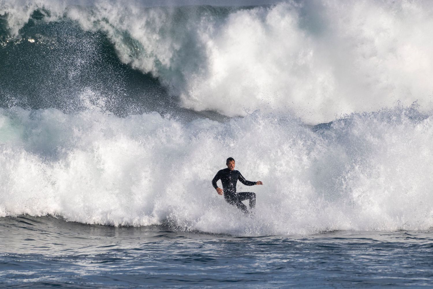 Surfer riding through massive crashing wave with dramatic white spray.