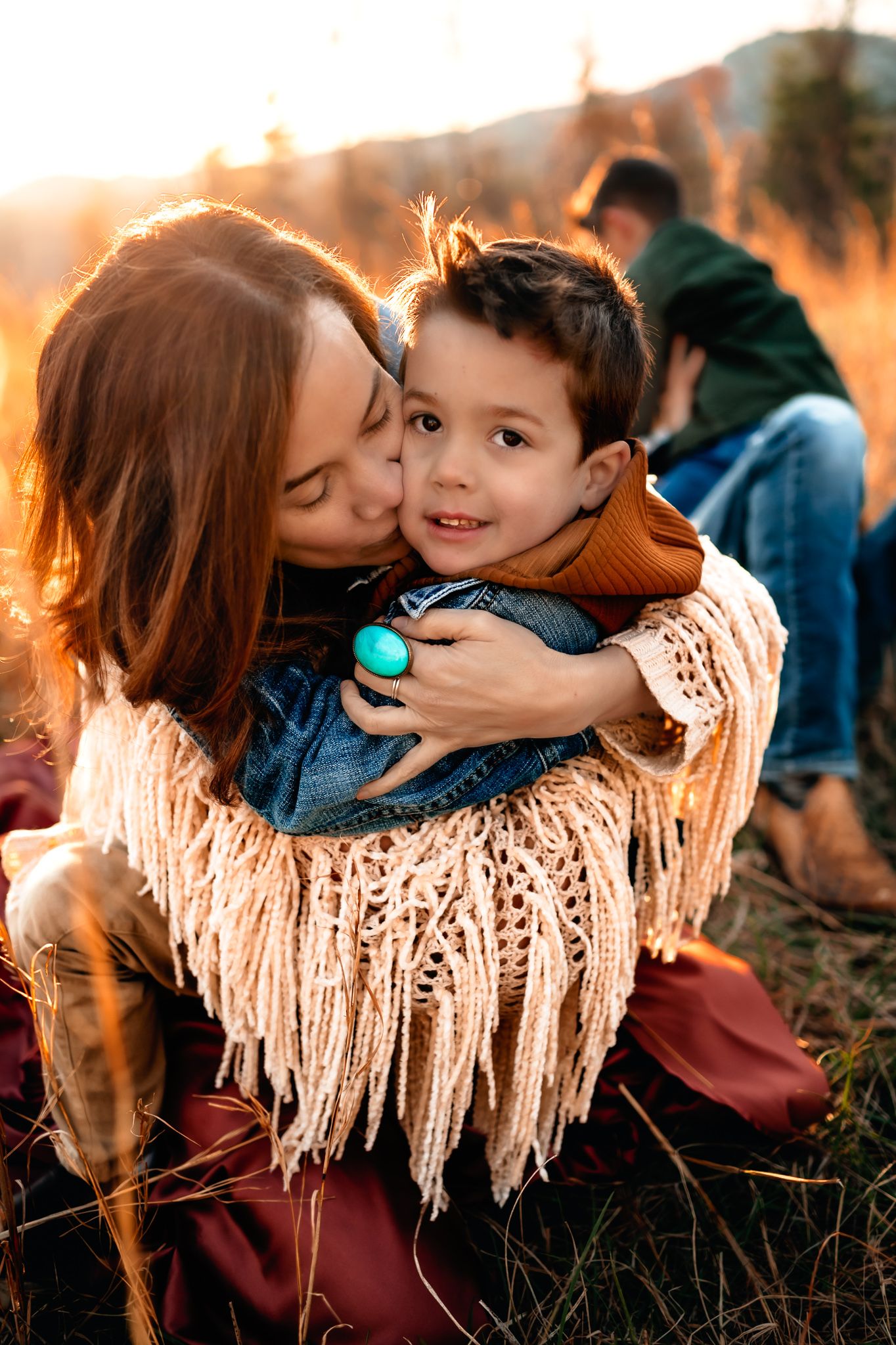 Tender embrace between family members wearing a fringed shawl in warm sunset lighting.