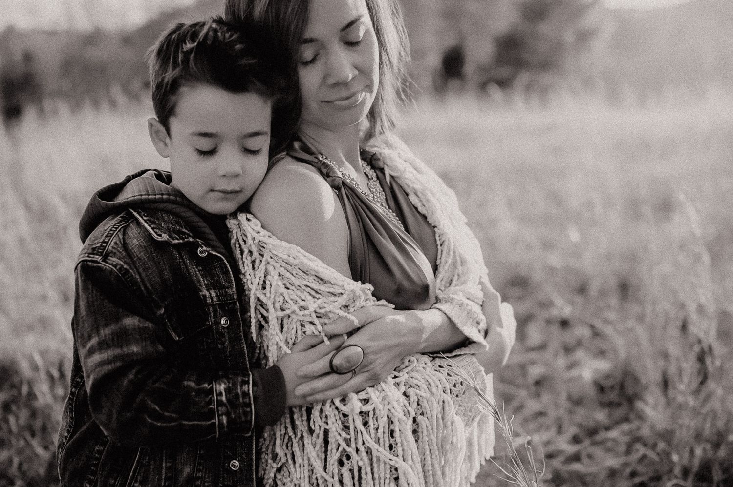 Black and white intimate portrait of parent and child in field wearing casual outfits.