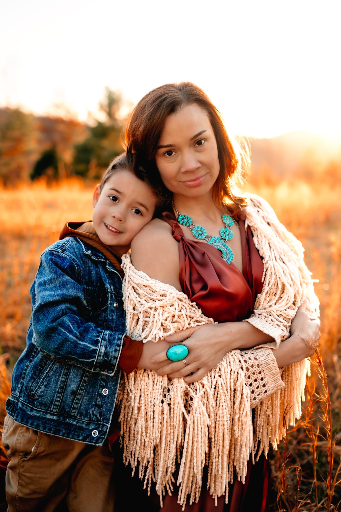 Intimate family portrait in autumn field with burgundy dress and fringed shawl against sunset.