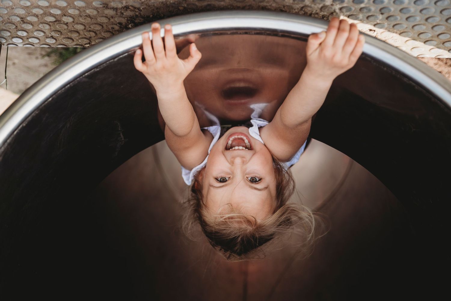 Small child hanging upside down inside a metal tunnel or tube.