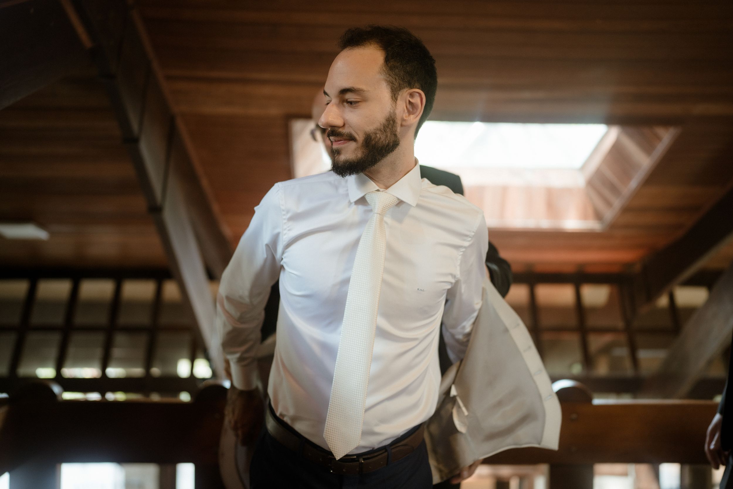 A person in formal attire smiles while getting ready in a rustic wooden room.