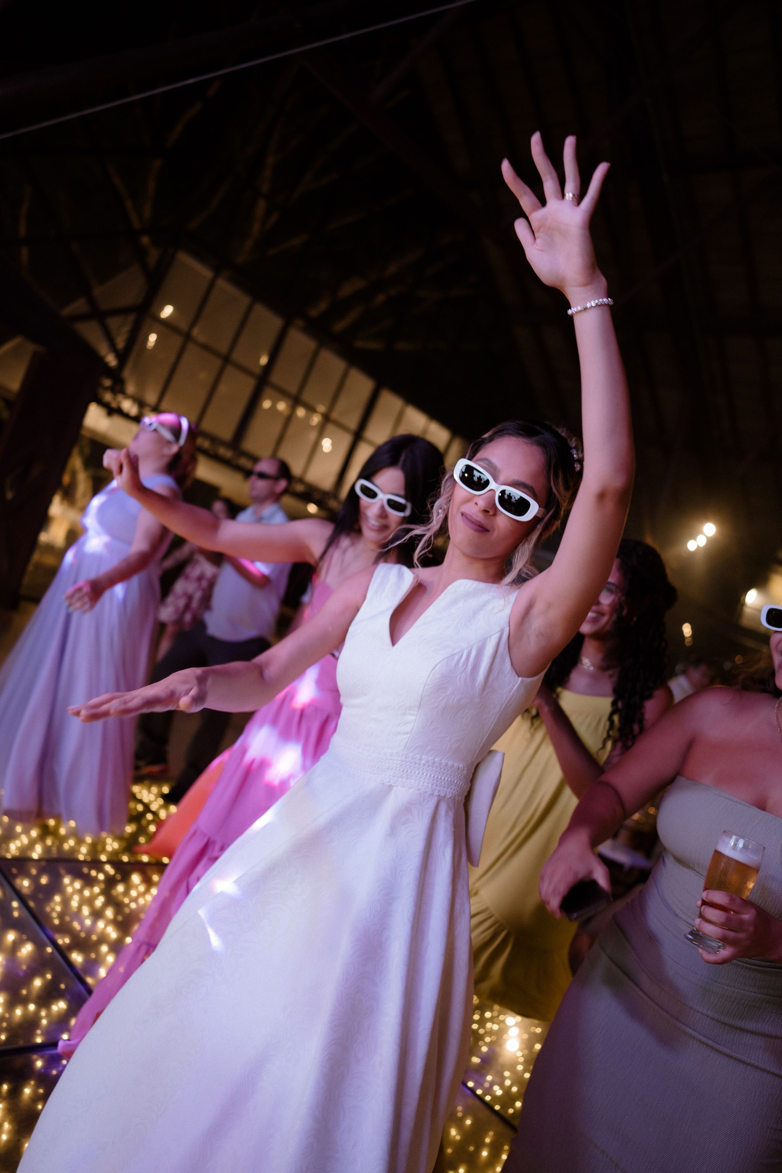 Wedding celebration with dancers wearing sunglasses and having fun under pink lighting.