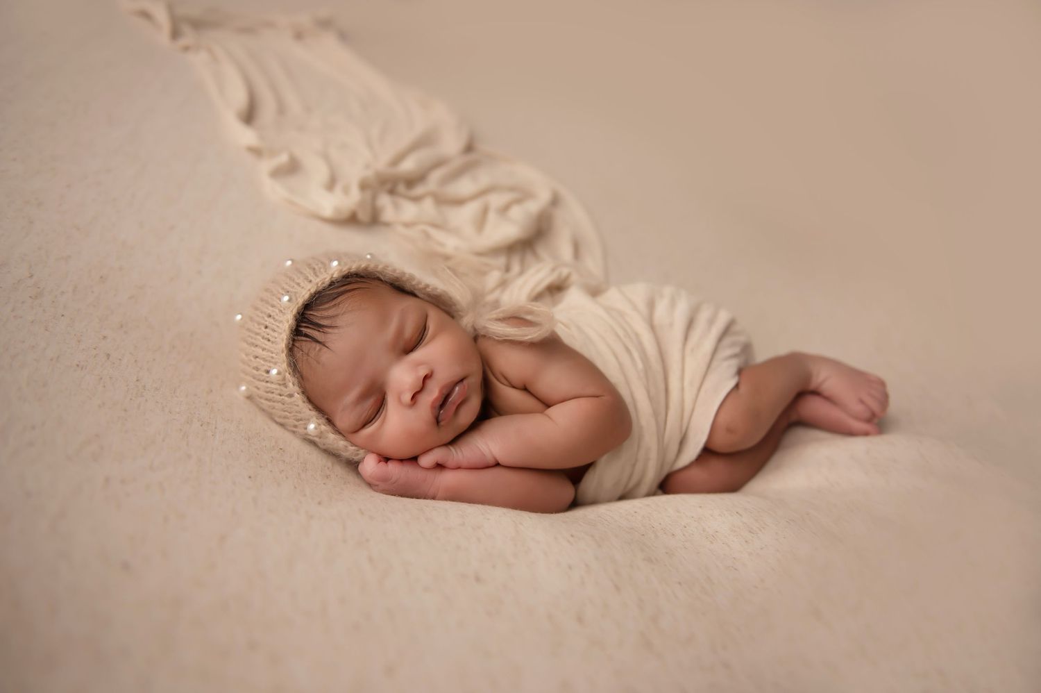 Sleeping newborn wrapped in cream fabric on soft textured background.