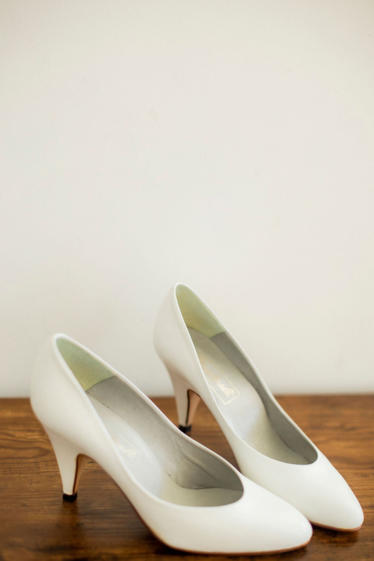 Classic white bridal pumps with medium heel displayed on wooden surface.