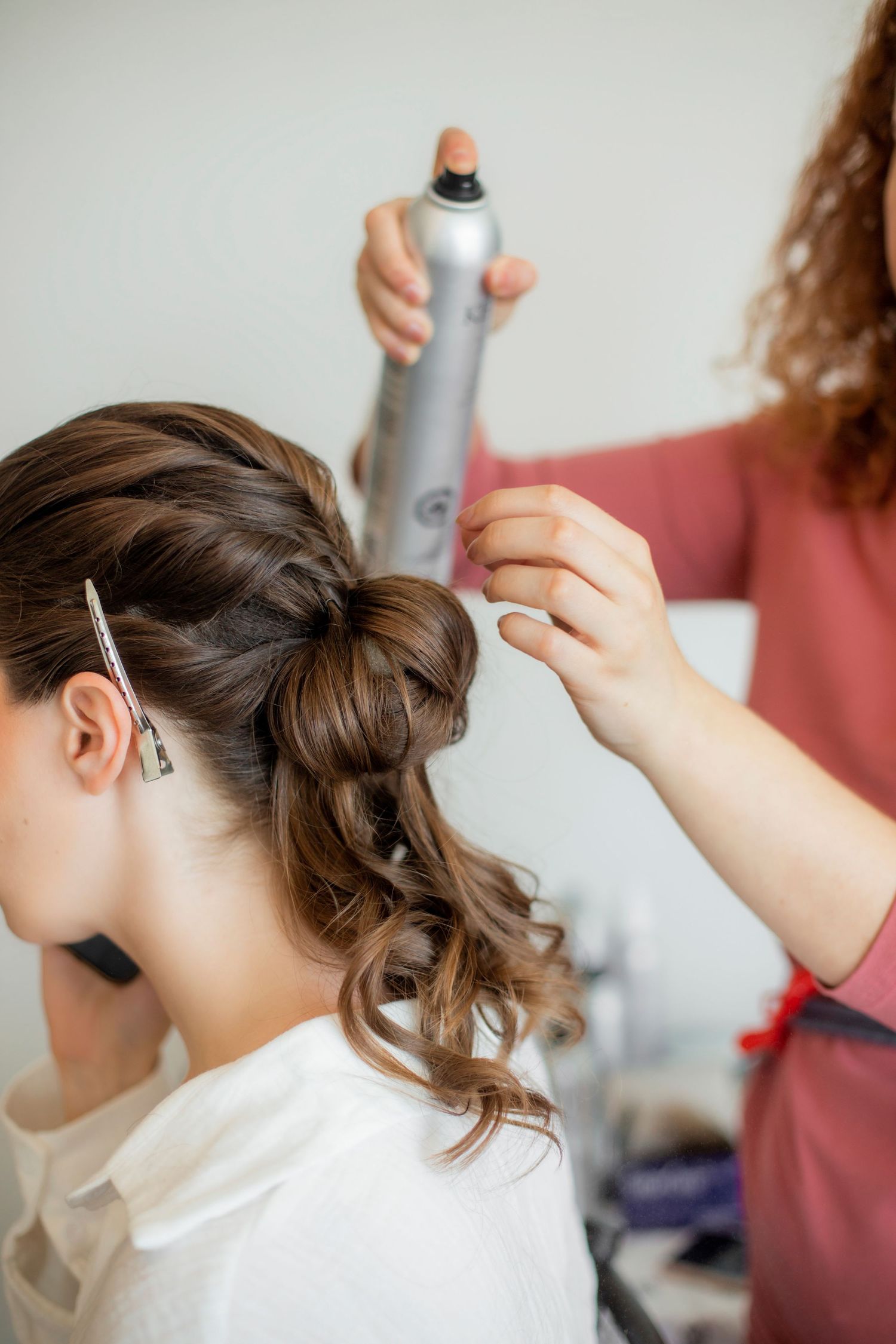 Stylist applying hairspray to elegant updo hairstyle in preparation.