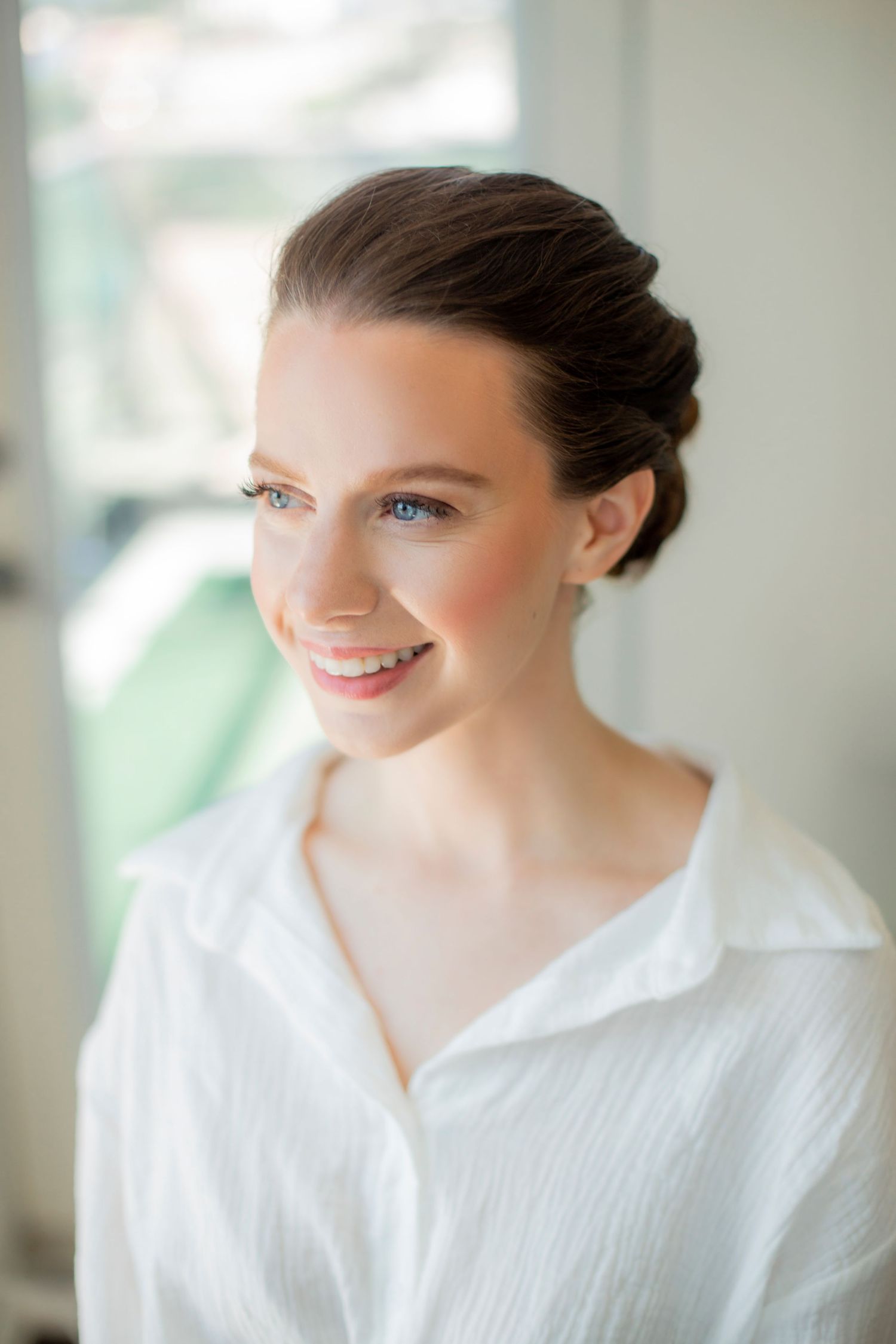 Classic bridal portrait with elegant updo and natural makeup by window.