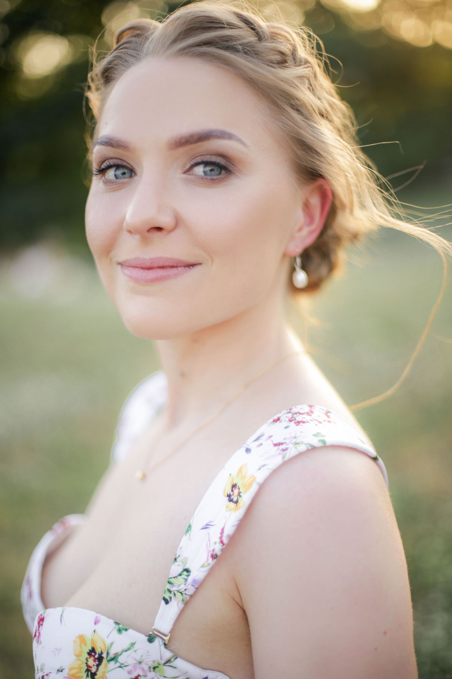 Portrait in golden sunlight wearing a floral dress and elegant updo hairstyle.