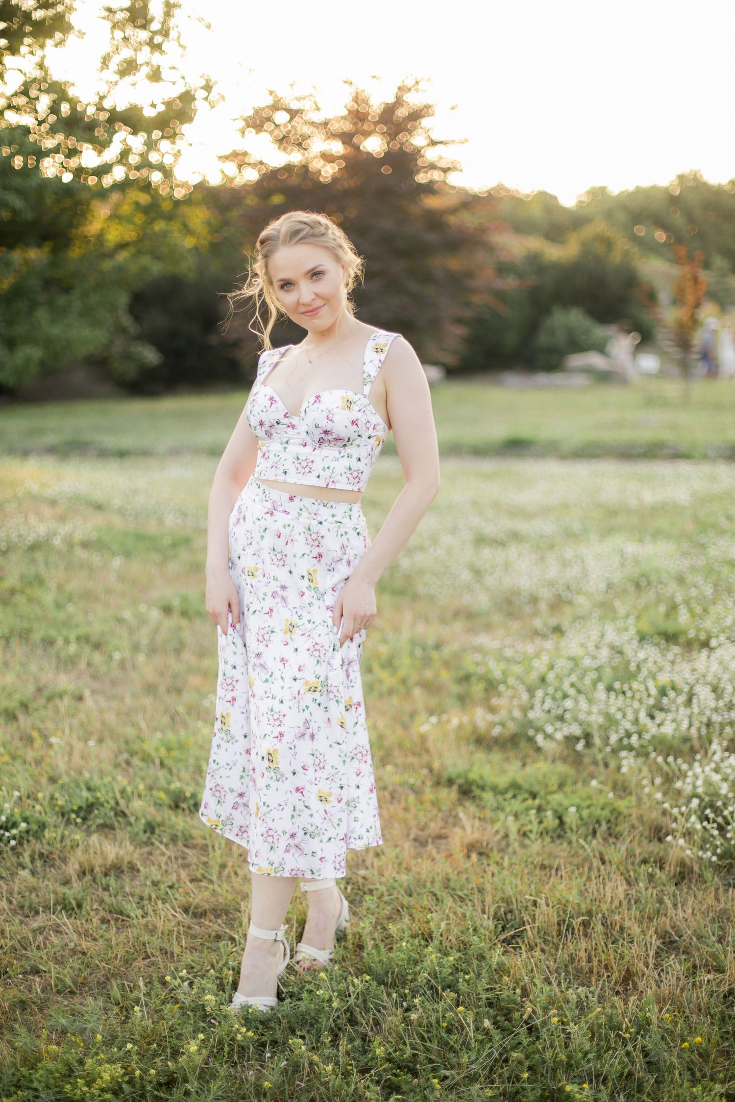Summer portrait in a floral dress standing in a grassy field at sunset.