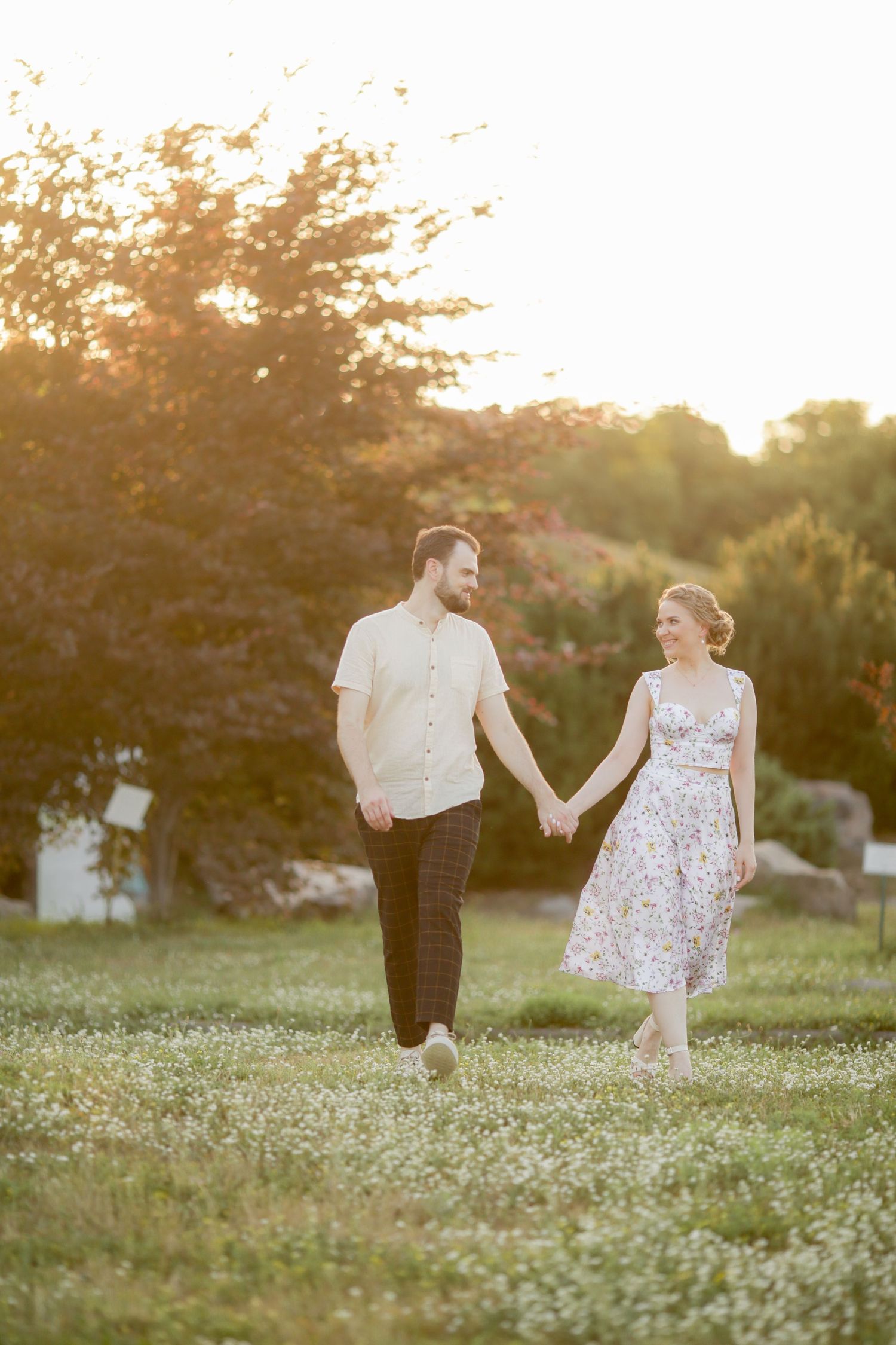 Couple walking hand in hand through a meadow at sunset.