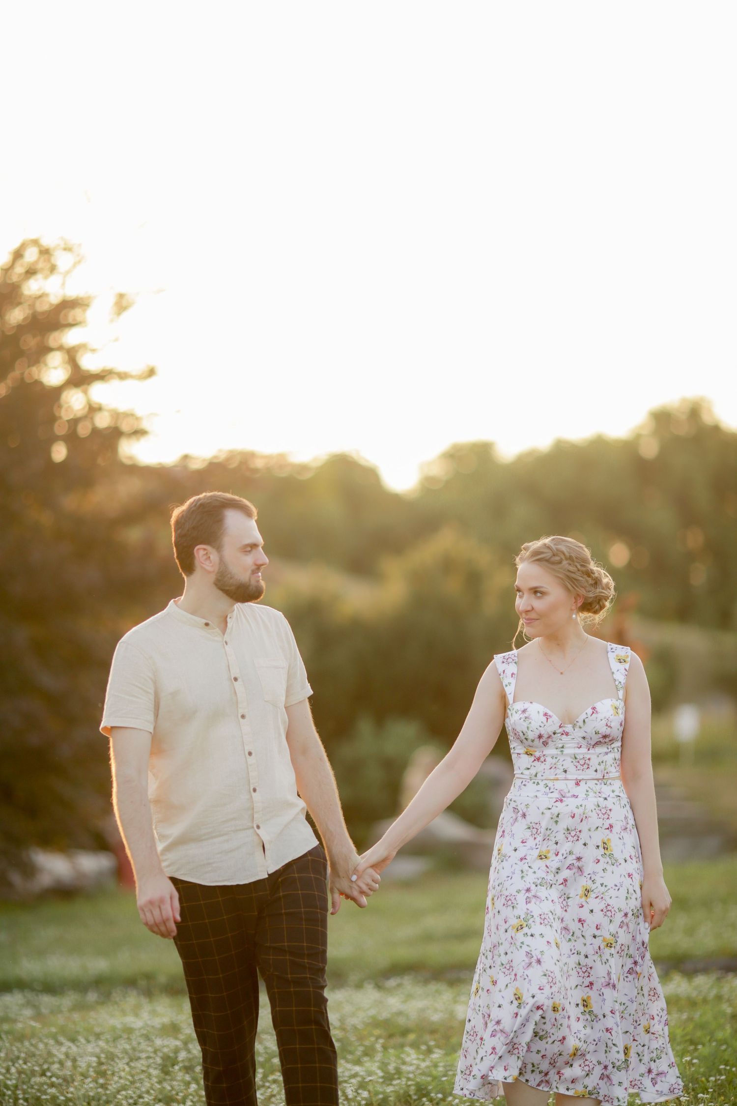 Couple holding hands in a romantic sunset photoshoot outdoors wearing coordinated white and floral outfits.