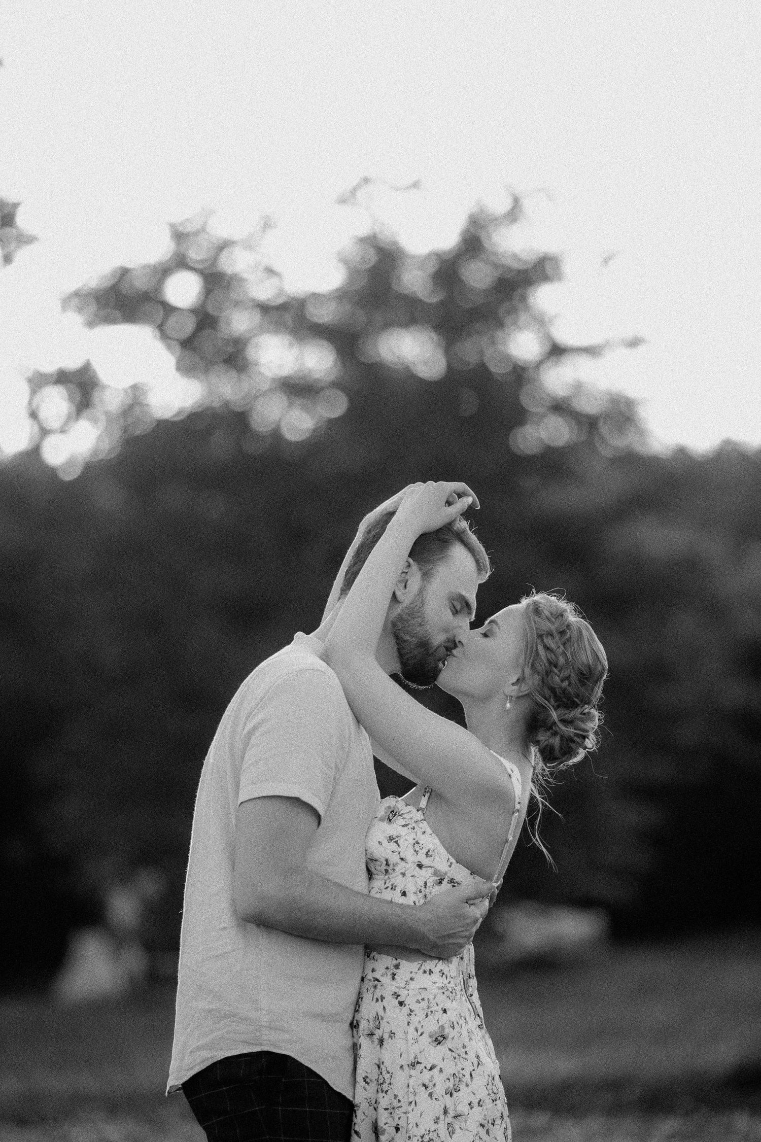 Black and white portrait of a couple embracing outdoors with bokeh background.
