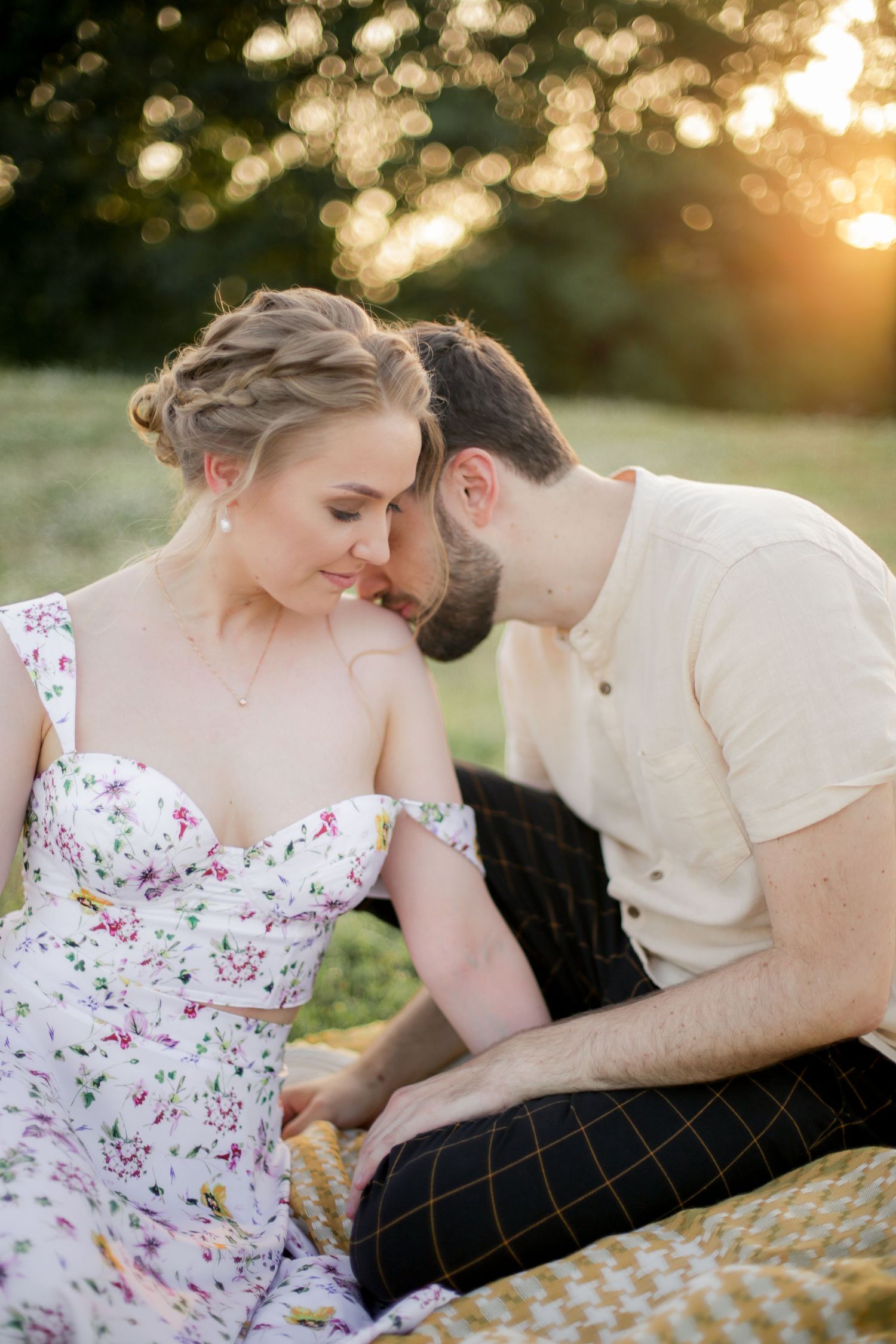 Intimate golden hour portrait of couple sitting close together on picnic blanket in field.